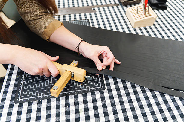 Artisan using a wooden strap cutter to slice a strip of black leather on a checkered workbench. High quality photo