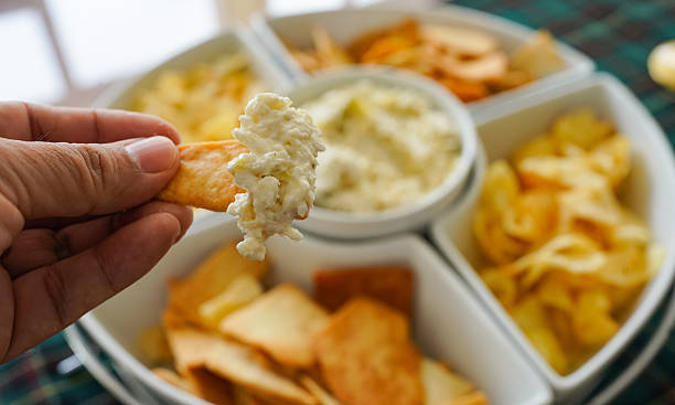 istock Hand dipping cracker into creamy artichoke dip at party 2253076031