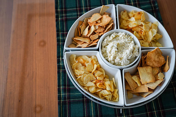 Artichoke dip in a white serving dish surrounded by potato chips and pita bread on a table