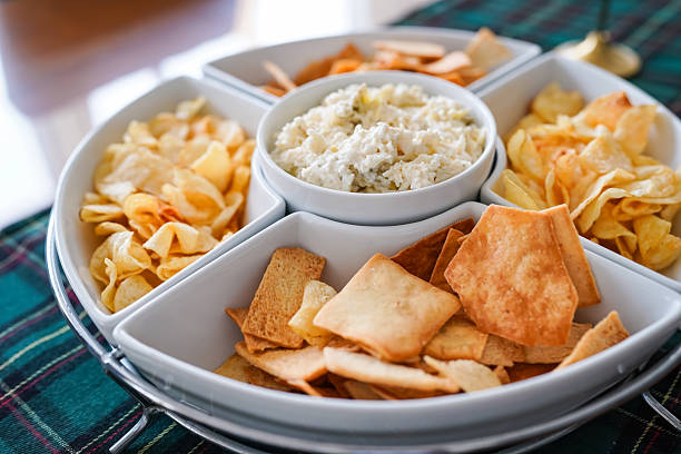 Artichoke dip served with potato chips and crackers on a white serving platter