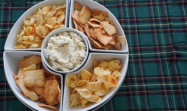 Artichoke dip served with potato chips and pita bread on a festive plaid tablecloth
