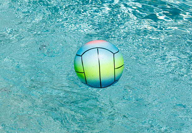 A colorful ball is floating in a pool. The ball is green, yellow, and blue. The water is clear and calm