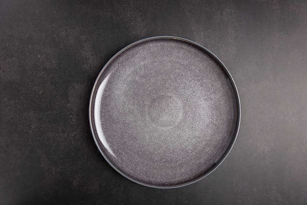 istock Dark gray ceramic plate on black textured background with copy space, top view and minimalist style. Neutral and modern composition for branding, advertising and design projects. Concept of minimalist tableware and modern lifestyle 2253082321