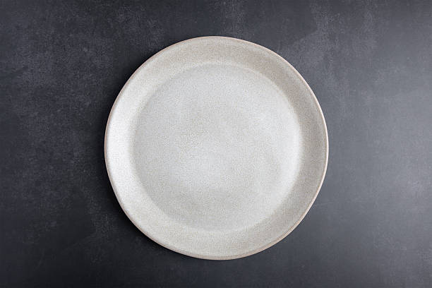 istock Empty beige ceramic plate on dark background with copy space, top view. Minimalist composition for food branding, menus or graphic design. Concept of minimalist tableware and modern design 2253082332