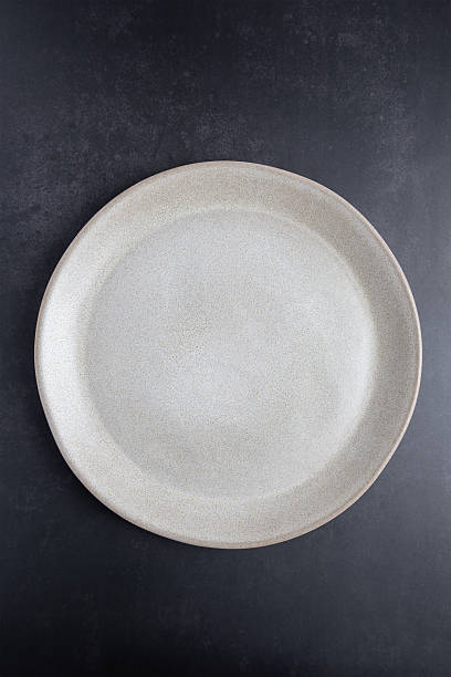 istock Beige ceramic plate photographed from above on a dark background, vertical format with copy space. Minimal style image for editorial, creative or lifestyle projects. Concept of simple dining and contemporary lifestyle 2253082337