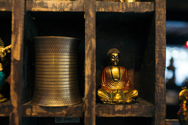 Golden buddha statuette sitting inside a wooden display shelf next to an ornate metal vessel