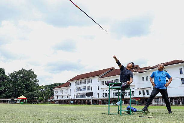 Paralympian Athlete with Leg Amputee Throwing Javelin with Coach on Grass Field at Sports Training