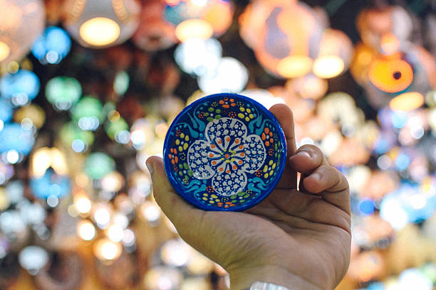 Hand holding colorful turkish ceramic bowl with blurred lanterns in the background