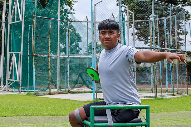 Young Disability Athlete Throwing Frisbee While Seated on Green Chair Outdoors