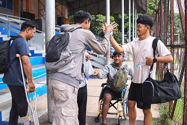 Young Men Greeting Each Other with High Fives at Sports Stadium, Showcasing Friendship and Camaraderie Among Athletes with Diverse Abilities