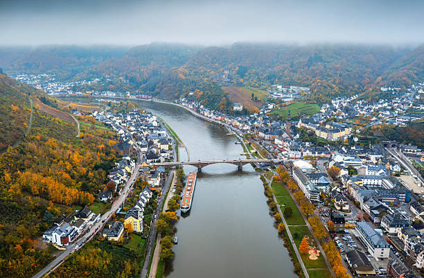 Aerial viewt of the historic town of Cochem an der Mosel along the Moselle River, Germany, featuring the river bridge, boats, vineyards, and surrounding hills with colorful autumn foliage. The scenic landscape highlights traditional architecture, river tourism, and the rural charm of the Mosel wine region in Rhineland-Palatinate. Cochem in Rhineland-Palatinate, Germany - Europe