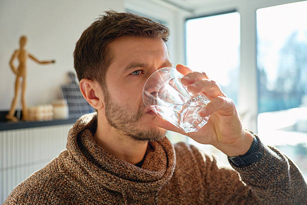 istock Man drinking water from glass in home kitchen closeup 2253096754