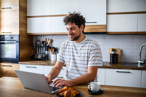 istock A smiling man eats a croissant while working on his laptop at home, representing a relaxed and productive remote work lifestyle 2253097538