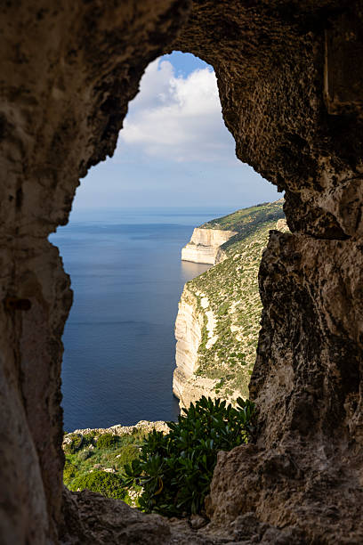 View of the Dingli Cliffs on the west coast of Malta seen through a natural rock opening, overlooking the deep blue Mediterranean Sea and dramatic limestone coastline.