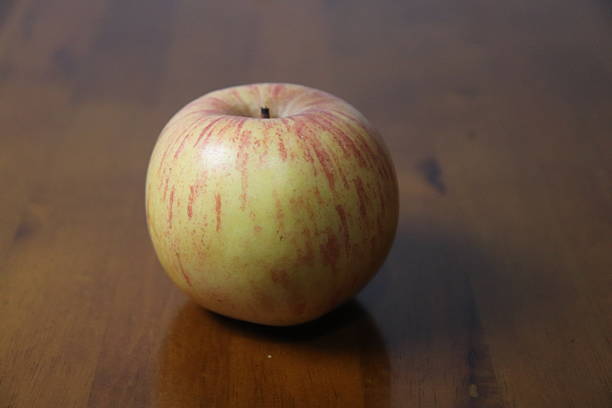 Fresh, single apple with red streaks rests on a polished brown wood background, creating a simple still life composition