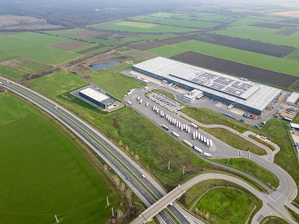 istock Aerial view of a large logistics warehouse with loading docks and trucks, distribution center surrounded by farmland. Supply chain and transportation concept 2253103862