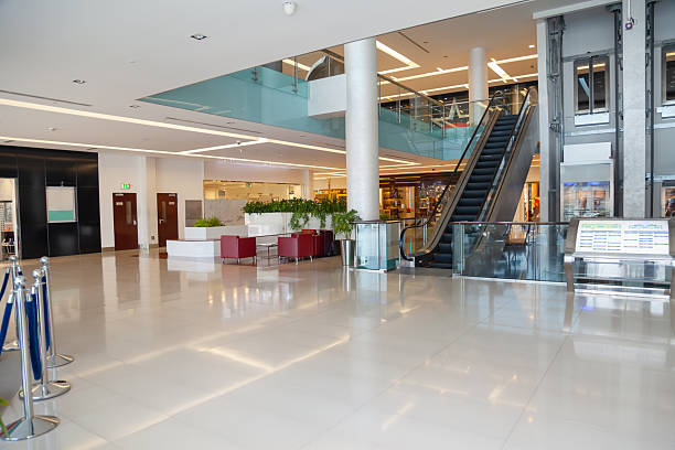 Bright and spacious interior of a modern shopping mall featuring an empty corridor with polished floors, glass railings, escalators, and minimalist architectural design The scene represents a quiet retail environment during off hours and can also resemble a public interior such as an airport terminal, hospital lobby, business center, or hotel atrium Ideal for concepts related to retail, real estate, commercial architecture, urban lifestyle, copy space, and modern infrastructure