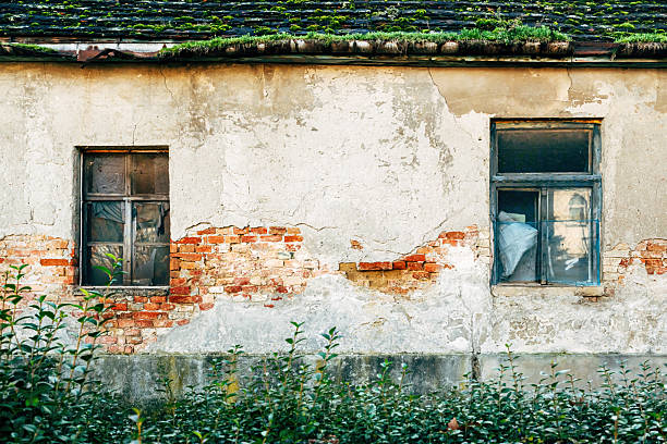A quaint window reveals a delicate white curtain, framed by a rustic wall. Bright red geraniums bloom in terracotta pots, adding a splash of color to the serene exterior.