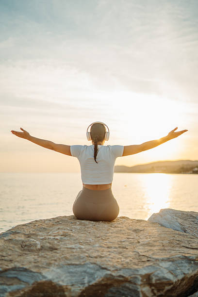 istock Woman meditating on rock enjoying sunset ocean view 2253113045