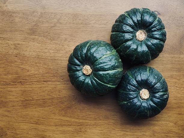 Green, spotty pumpkin with dry tail against blurred, light background. Close up of shaped, ripe pumpkin, with sunlight reflection on hard skin at sunny autumn day. Harvesting, vegetables concept.