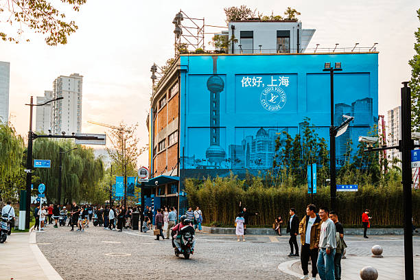 Shanghai, China - October 14, 2023: A lively Shanghai street scene featuring a bold blue mural on a building, with pedestrians, cyclists, and visitors enjoying a sunny day in a modern urban plaza.