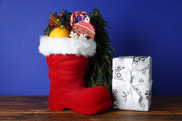 istock Happy Saint Nicholas day. Red boot with sweets, festive decor and gift box on wooden table against blue background 2253114399