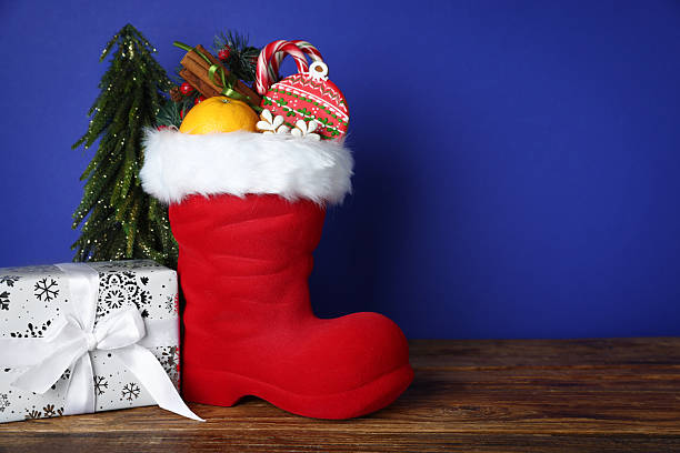 istock Happy Saint Nicholas day. Red boot with sweets, festive decor and gift box on wooden table against blue background. Space for text 2253114405