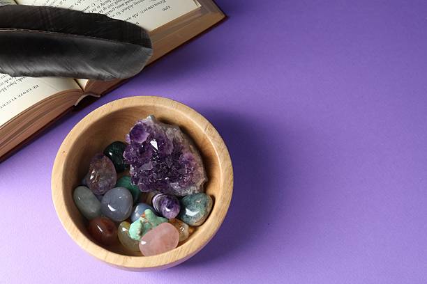 istock Different beautiful gemstones in bowl, feather and book on purple background, flat lay. Space for text 2253114605