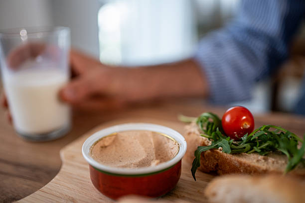 Person holding a glass of milk, preparing to enjoy breakfast or an appetizer of liver pate on toast, topped with fresh arugula and a cherry tomato, offering a delicious and rustic meal