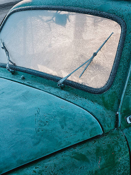 Close-up of frosted windshield and hood on a classic vehicle, warm morning light illuminates the cabin from behind.