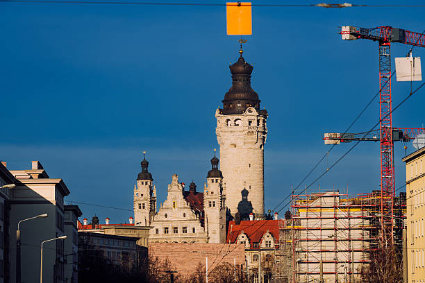 Leipzig cityscape featuring a tall historic tower amid scaffolding and cranes, set against a deep blue sky. A blend of old architecture and modern construction symbolizes growth and urban development in Germany.
