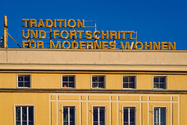 A bright yellow building with a bold sign reading Tradition and Progress for Modern Living against a clear blue sky in Leipzig, Germany. Urban architecture highlighting heritage and contemporary housing aesthetics.