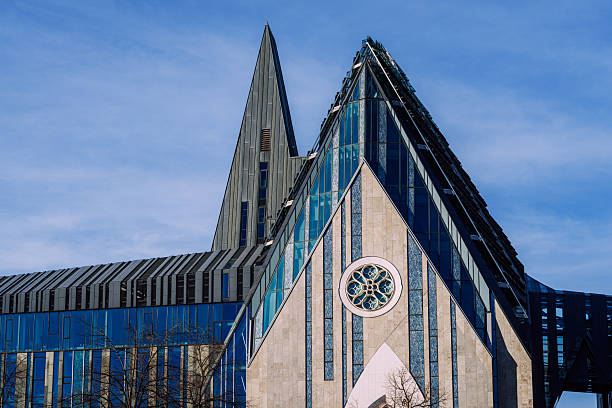 Leipzig's striking modern glass architecture features sharp triangular facades and a tall spire against a clear blue sky. A dramatic, contemporary building scene showcasing design, geometry, and urban texture.