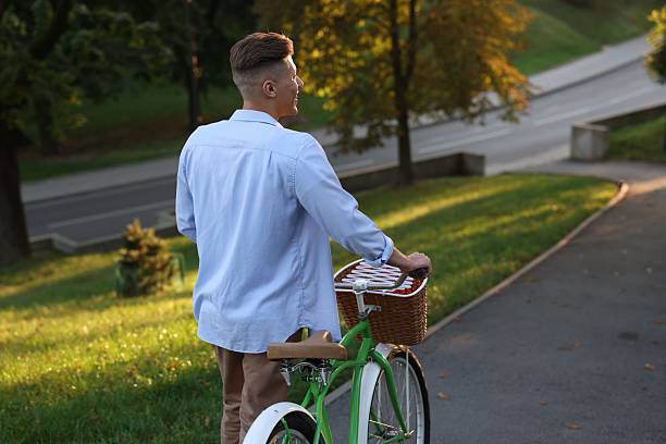 istock Happy man walking his bicycle in park on sunny day, back view 2253118375