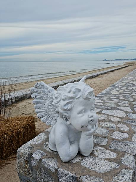 Cupid statue on a bench by the sea, with gentle waves and a serene horizon in the background. A romantic and peaceful scene, ideal for love, travel, and art-themed projects.