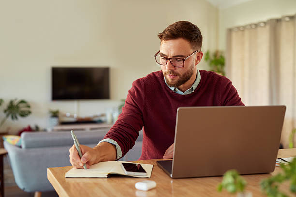istock Mid adult casual man writing notes while working at home 2253120090
