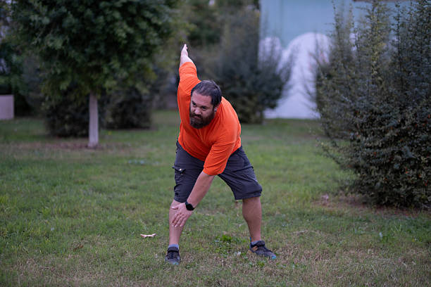 Outdoor workout scene with fat man. Healthy lifestyle concept: man working out outdoors. Fat man exercising in public park.