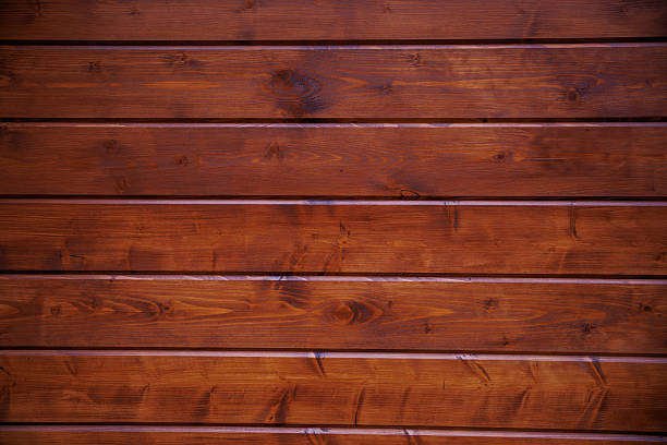 Horizontal wooden boards show knots, grain swirls, and tongue and groove seams. Warm reddish brown stain and semi gloss coat present with soft daytime reflections.