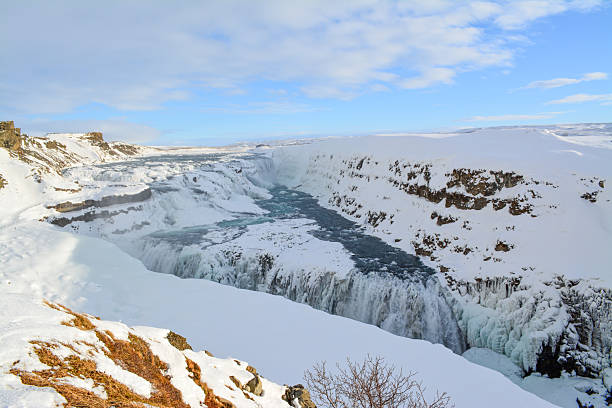 Icy canyon waterfall carving frozen landscape, turbulent river slicing through snowcovered cliffs with mist spray and turquoise pools, rugged rim and steep