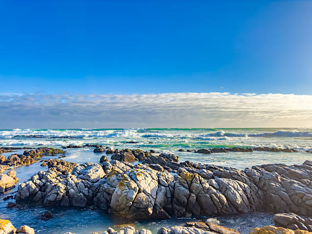Tranquil coastline landscape with azure sky, sand, rocks, and gentle waves, South Africa