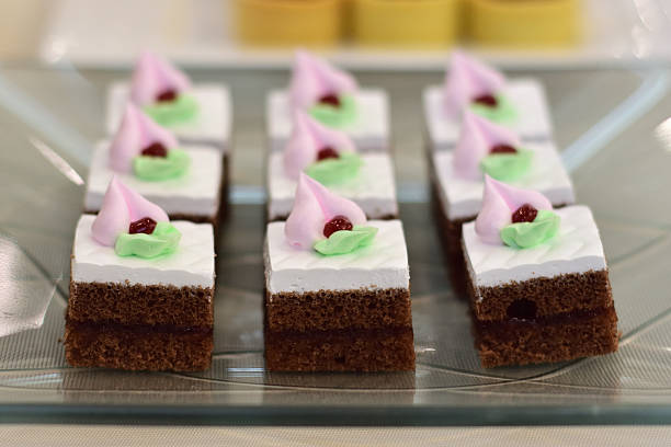 A plate of small chocolate cakes topped with pink frosting and green leaves, garnished with a cherry