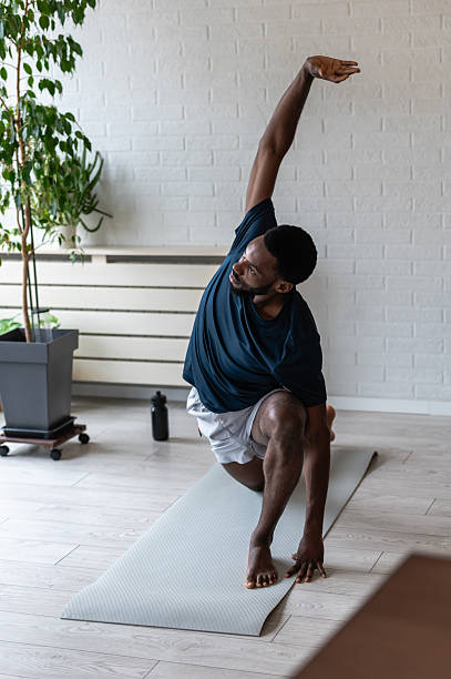 istock Fit man stretching on a yoga mat at home, performing a side bend exercise after workout in a bright modern living room with plants, focused on flexibility and healthy lifestyle 2253133541