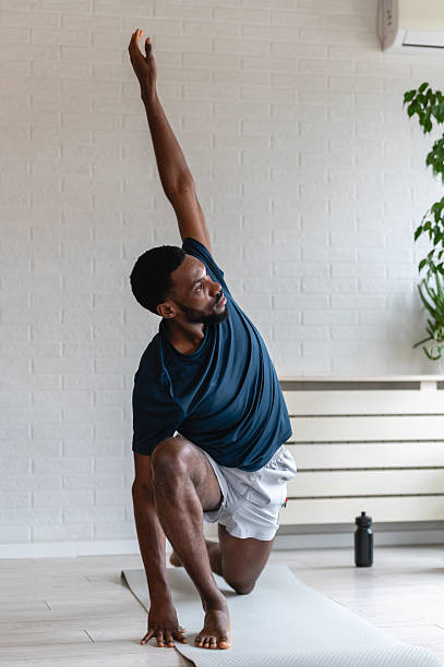 istock Fit man stretching on a yoga mat at home, performing a side bend exercise after workout in a bright modern living room with plants, focused on flexibility and healthy lifestyle 2253133550