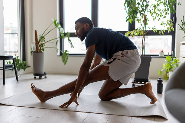 istock Focused Black man stretching hamstrings during yoga practice at home, reaching toward extended leg on a mat, calm and determined emotion in a bright, modern interior with plants 2253133771