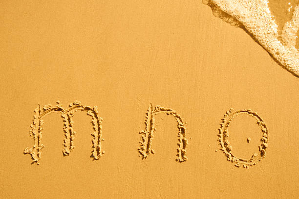 alphabet letters m n o handwritten in sand on beach
