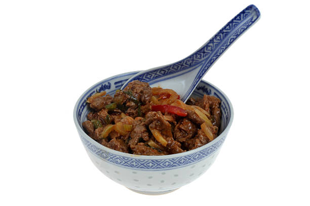 Bowl of beef meat with vegetables with a spoon close-up isolated on white background
