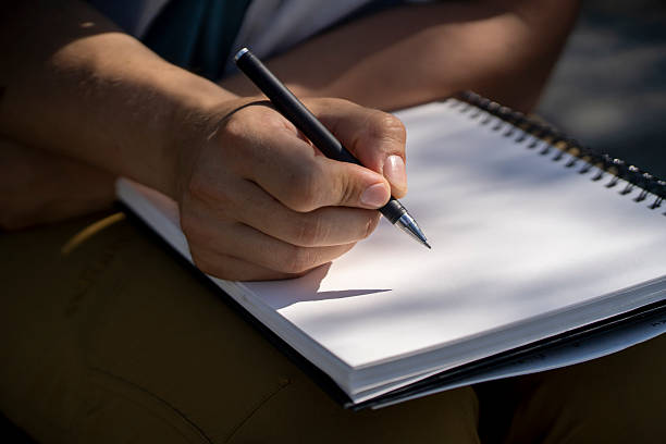 istock A male hand holds a pen and writes in a sketchbook, notepad closeup. 2253140511