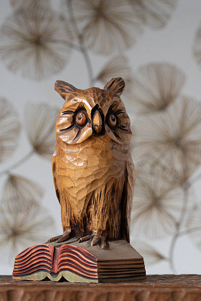 Wooden owl figurine standing on an open book on a wooden surface.