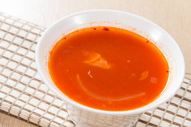 A white bowl of spicy red soup with visible oil layer, served on a woven mat.
