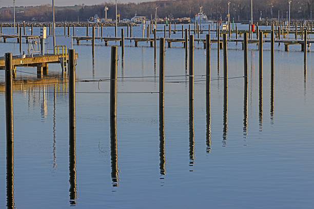 Vertical marina poles reflected in calm harbor water creating a minimalist composition.